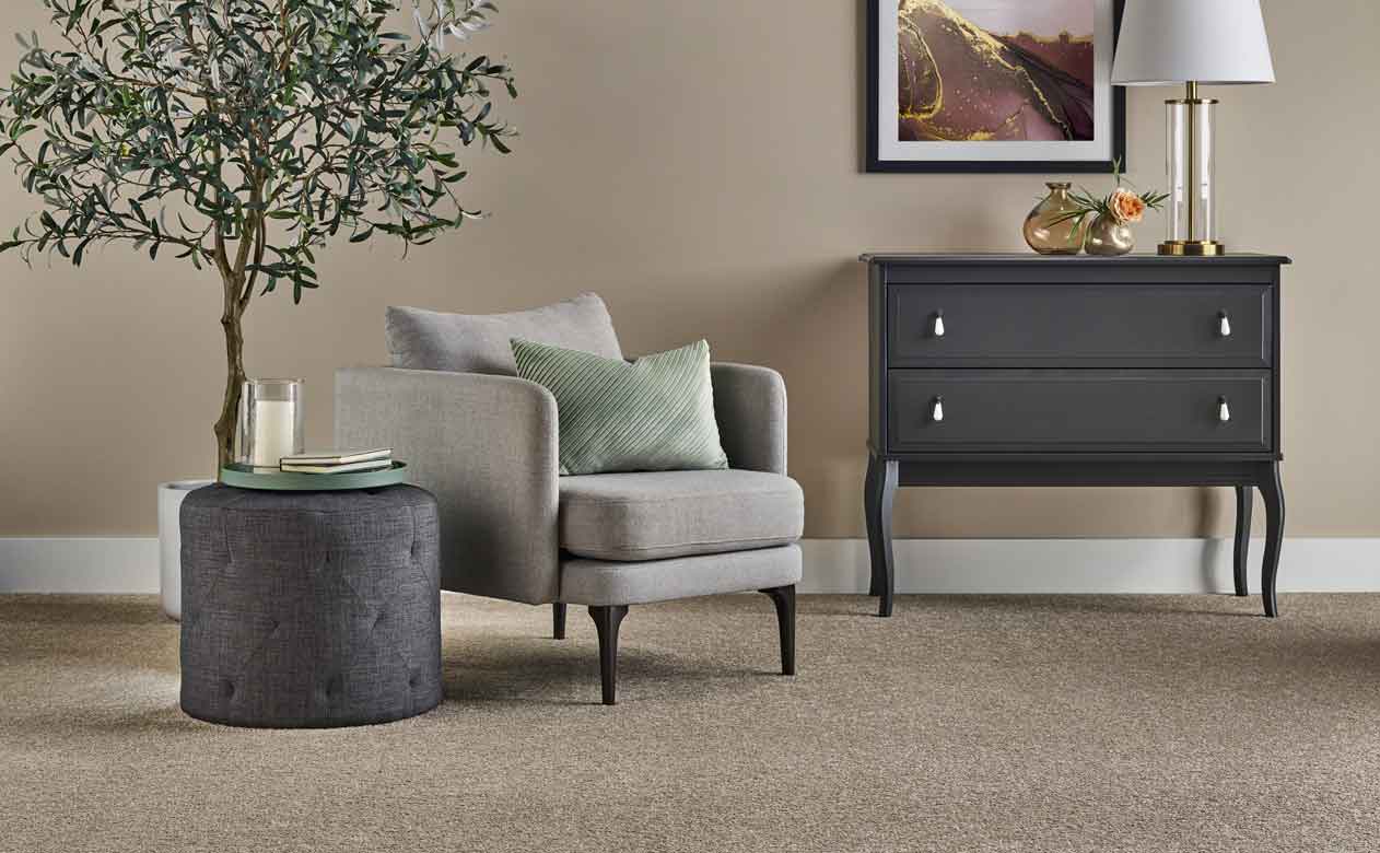 Living room with brown chair, ottoman, and dresser with beige carpet